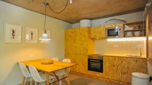 Une cuisine compacte avec des meubles en bois, un four à micro-ondes et un évier. On y trouve une table à manger avec des chaises et des tableaux encadrés accrochés au mur.