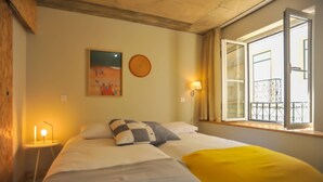Une chambre d’hôtel avec un lit, une lampe de chevet, un tableau au mur et une fenêtre donnant sur un balcon.