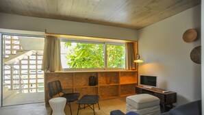 Un salon avec un plafond en bois, une grande fenêtre avec des rideaux, un téléviseur, un bureau et un canapé.