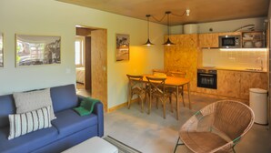 Un espacio habitable compacto con kitchenette, comedor y zona de estar con sofá y sillón.