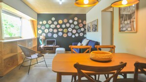Un comedor con una mesa y sillas de madera, una pared decorada con platos y un televisor al fondo.