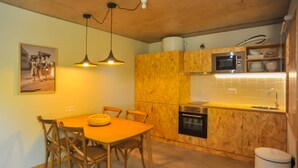 Una cocina con armarios de madera, un microondas y un lavamanos. Hay una mesa de comedor con sillas y una lámpara colgante.