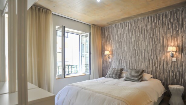 Un dormitorio con una cama grande, una ventana con cortinas, una lámpara fijada a la pared y un revestimiento texturizado.
