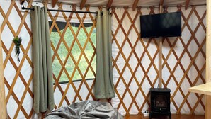 Une pièce chaleureuse avec un plancher en bois, un fauteuil poire gris, un tapis à motifs, un petit radiateur noir et un téléviseur fixé au mur.