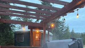 Un bain à remous avec un banc, une terrasse couverte et une petite cabane en arrière-plan.
