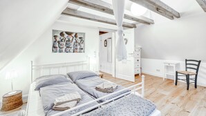 A bedroom with a bed, a chair, a desk, and a painting on the wall.