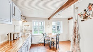 A kitchen with white cabinets, a wooden countertop, and a dining area with two chairs and a table.