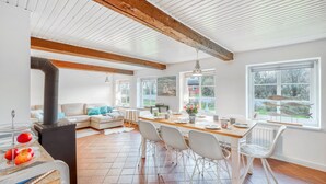 A spacious living area with a high ceiling, exposed wooden beams, a fireplace, and a dining area with a view of the outdoors.