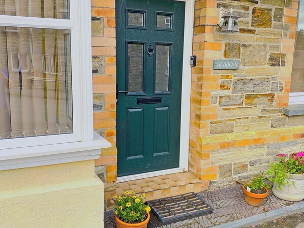 A green door with a nameplate, a window with curtains, and a stone wall with a birdhouse. - 1 bedroom accommodation in Llanboidy, Whitland (Llanboidy, Whitland)