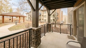 A covered outdoor area with a stone wall and metal railing, a bench, and a gazebo in the background.