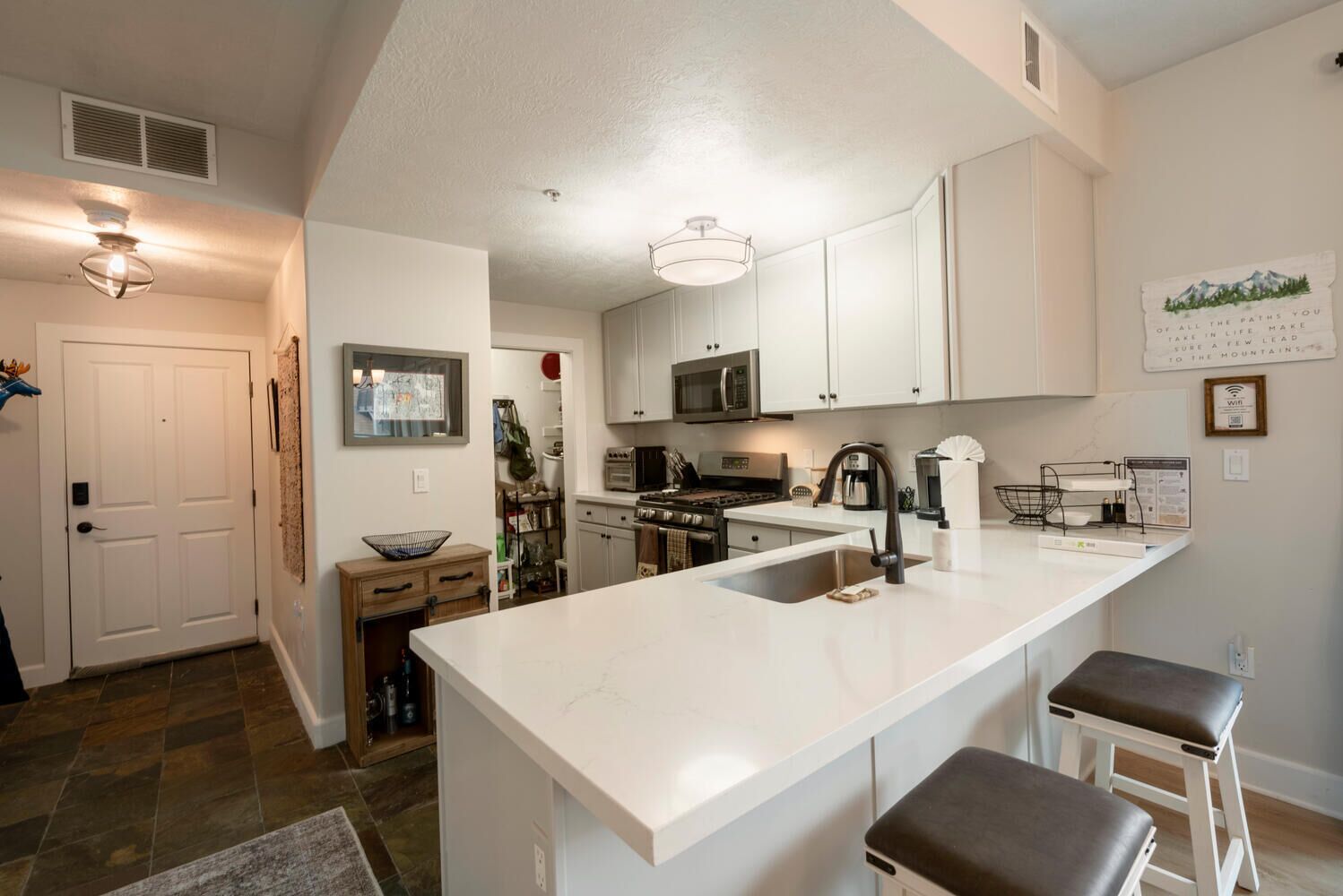 A modern kitchen with white cabinetry, a central island with stools, a microwave, and a stove.