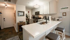 A modern kitchen with white cabinetry, a central island with stools, a microwave, and a stove.