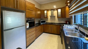 A modern kitchen with wooden cabinets, stainless steel appliances, and a black countertop. - Central Secured Compound w/ Hill-view Terrace (Amman)