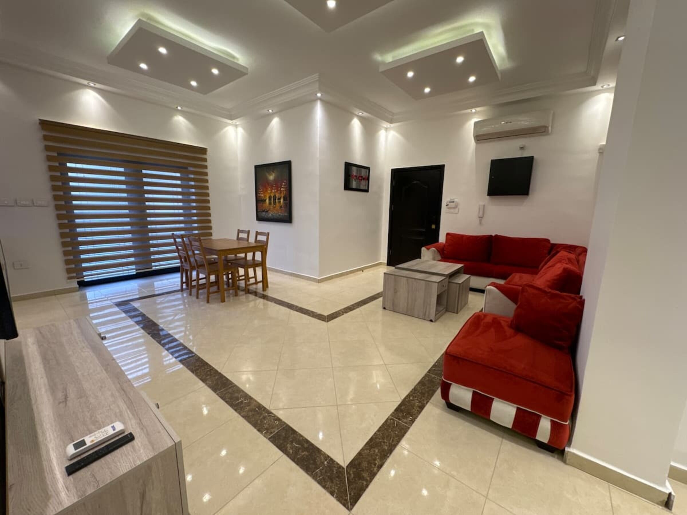 Una sala de estar moderna con comedor, un sofá rojo y un televisor montado en la pared.