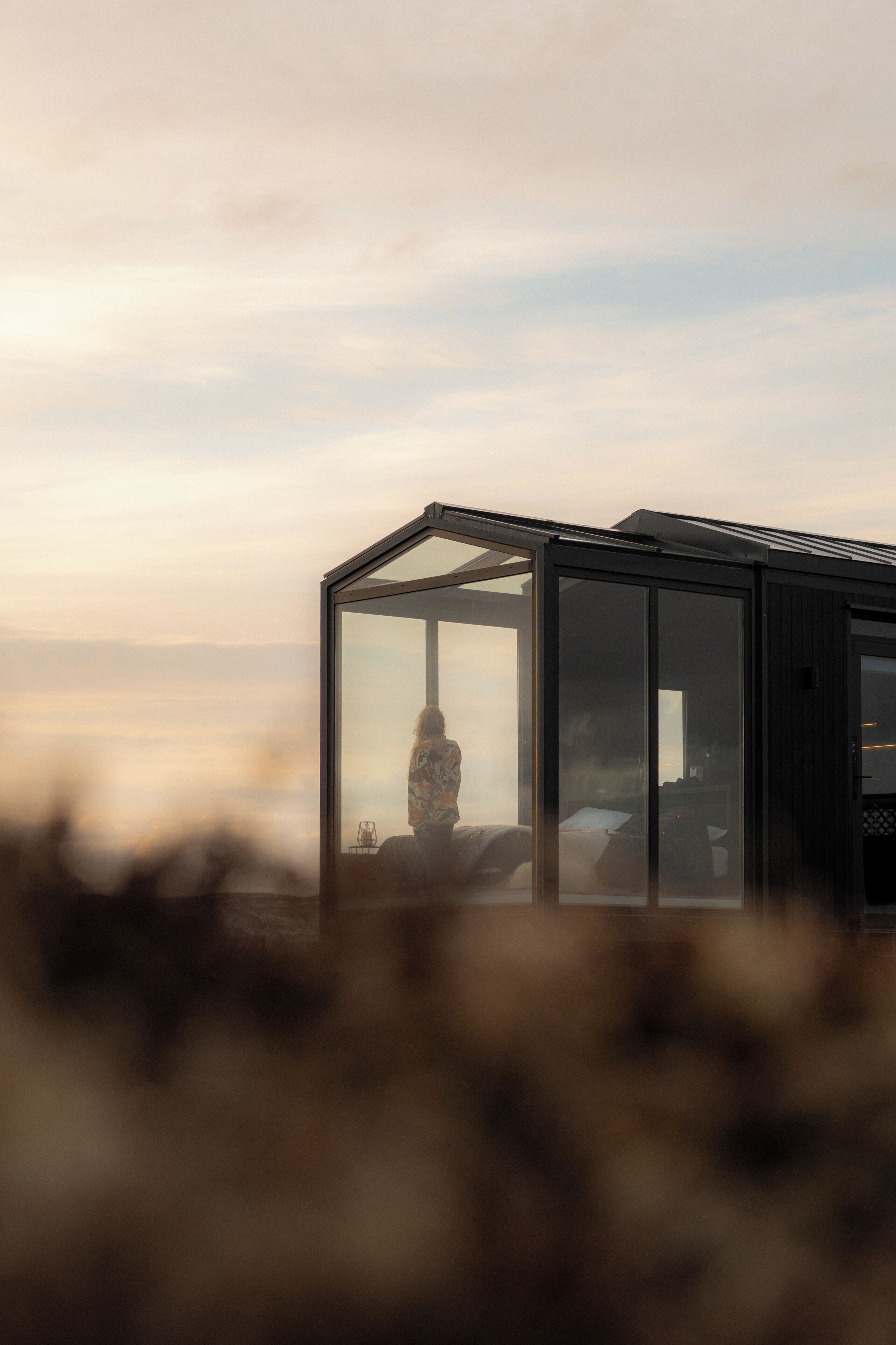 A modern glass structure with a person inside, possibly a room or a suite, with a view of the sky.