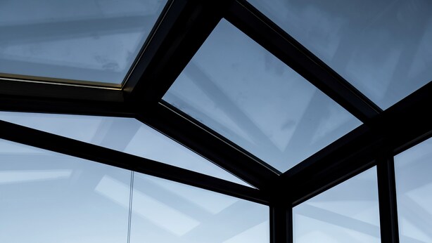 A person sitting on a bed in a room with large windows, a view of a snowy landscape, and a modern architectural design. - Tiny Glass Lodge (Selfoss)
