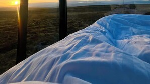 A room with a large window, a bed, and a view of the landscape. - Tiny Glass Lodge (Selfoss)