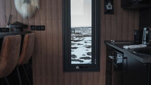 A modern kitchen with a view of a snowy landscape through a large window. - Tiny Glass Lodge (Selfoss)