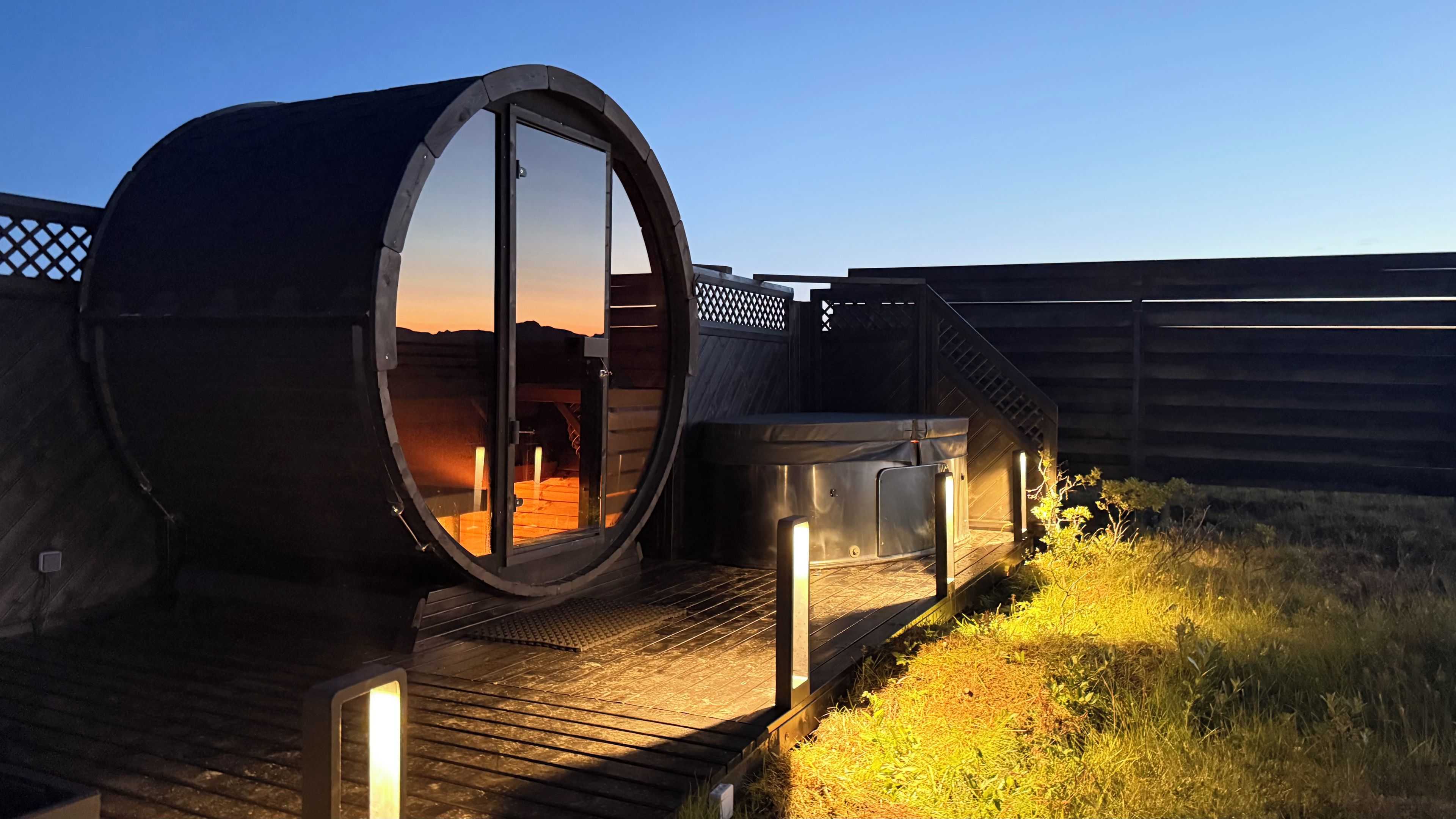 Una estructura cilíndrica con puerta de vidrio, terraza de madera e hidromasaje.