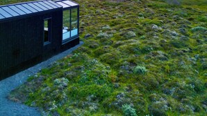 A modern building with a glass facade, situated in a grassy field with a distant mountain range and a colorful sky. - Tiny Glass Lodge (Selfoss)