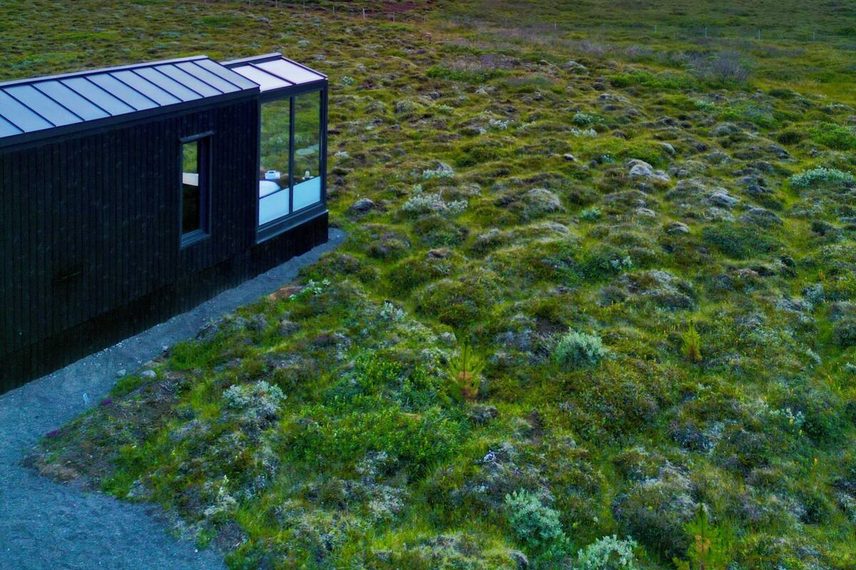 A modern building with a glass facade, situated in a grassy field with a distant mountain range and a colorful sky.