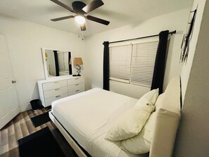 A bedroom with a bed, a ceiling fan, a dresser, a mirror, and a window with blinds.