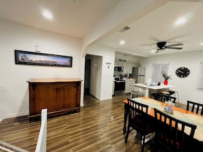 A modern kitchen with a microwave, stove, and refrigerator, a dining area with a wooden table and chairs, and a hallway leading to another room.