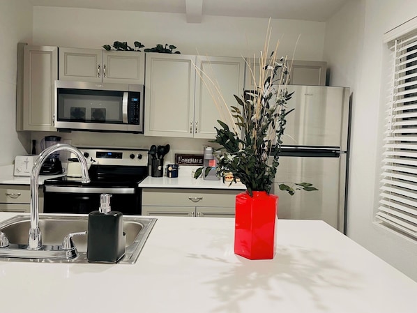A modern kitchen with white cabinets, stainless steel appliances, a red vase with greenery, and a 'Homemade' sign.