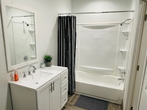 A bathroom with a white sink, mirror, and cabinet, a shower with a curtain, and a small potted plant.
