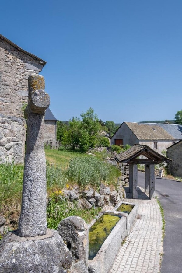 A stone structure with a unique head sculpture, a stone wall, and a paved pathway leading to traditional buildings.