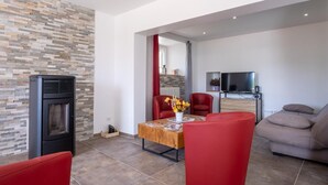 A modern living room with a fireplace, red chairs, a sofa, and a TV.