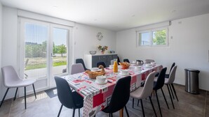 A dining area with a table set for four, chairs, a window with a view of greenery, and a trash bin.