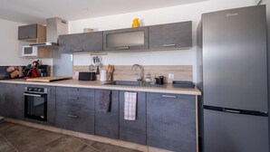 A modern kitchen with grey cabinets, a stainless steel refrigerator, and a wooden countertop.