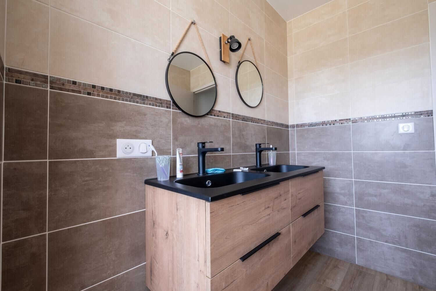Un baño con tocador de madera, dos grifos negros y dos espejos montados en la pared.