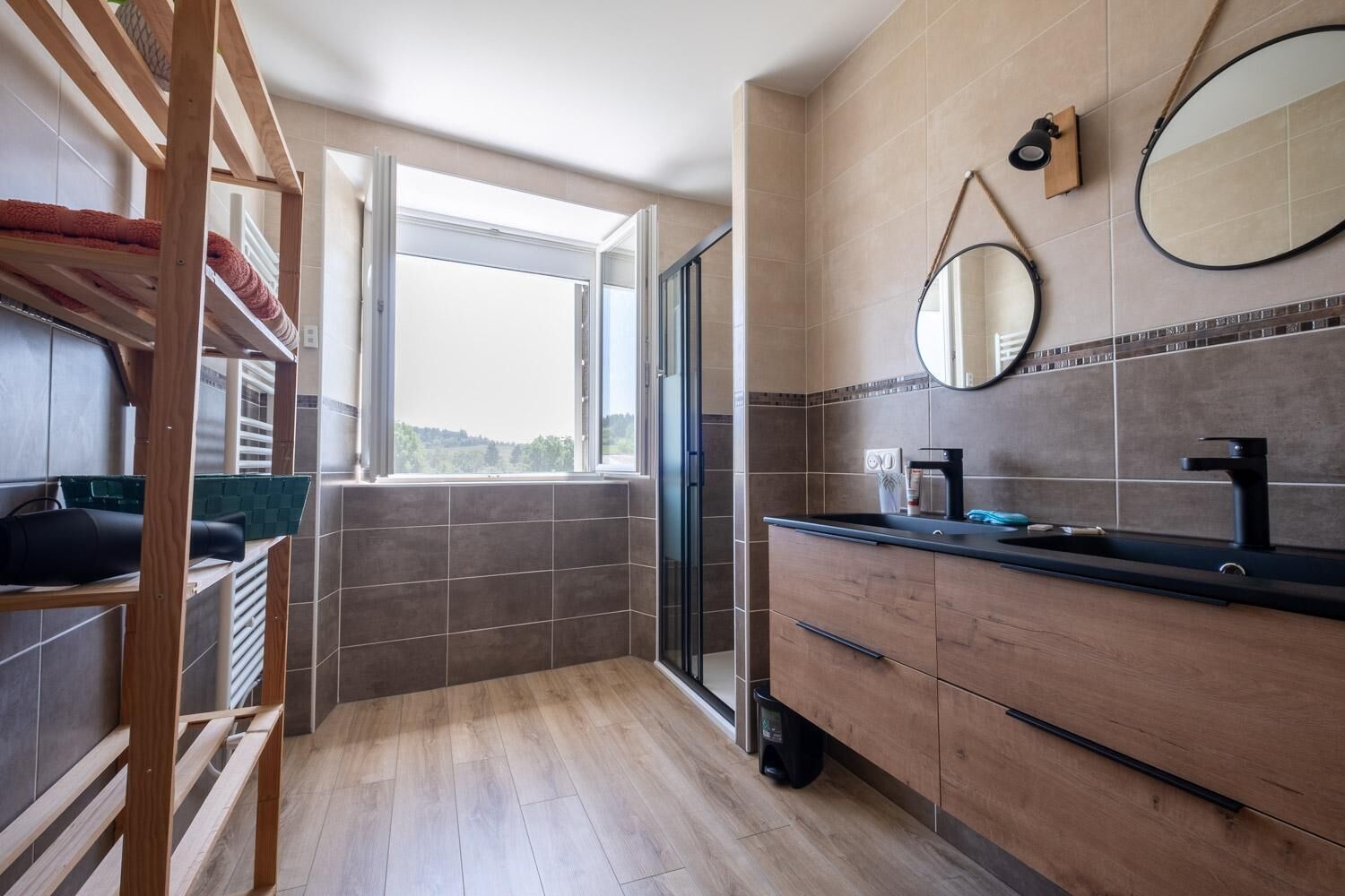 A modern bathroom with a wooden vanity, a large mirror, and a view of the outdoors through a window.