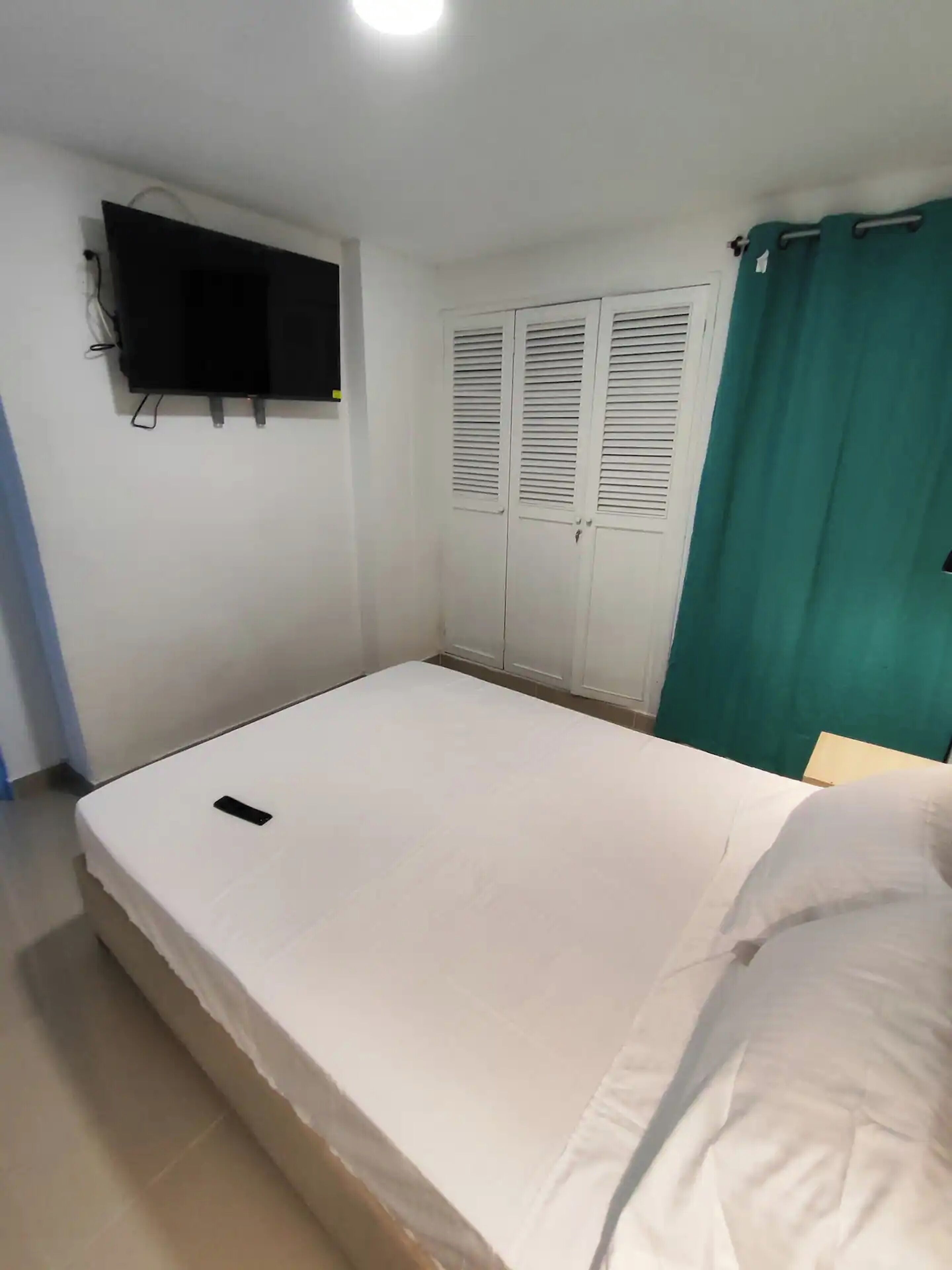 A bedroom with a bed, a TV mounted on the wall, and a set of wardrobes.