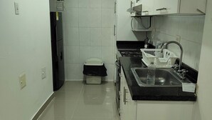 A small, modern kitchen with white cabinets, a black countertop, and a stainless steel sink.