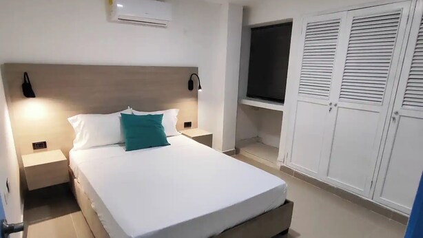 A bedroom with a bed, bedside tables, an air conditioner, a TV, and a wardrobe.