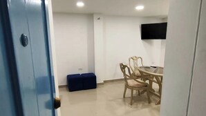 A room with a blue door, a round table with chairs, a blue bench, and a flat-screen TV mounted on the wall.