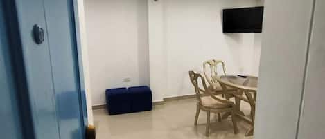 A room with a blue door, a round table with chairs, a blue bench, and a flat-screen TV mounted on the wall.