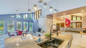 Una cocina moderna con encimeras de granito, un lavaplatos integrado y una zona de comedor con sillas rojas y una mesa.