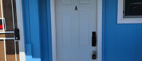 A white door with the letter 'A' above it, a window with a metal grill, and a blue wall with a white trim.