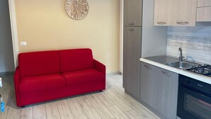 A modern kitchen with grey cabinets, a red sofa, and a wall clock.