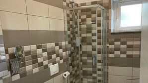 A bathroom with a shower, toilet, bidet, and a small stool.