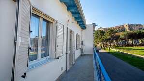 A building with white exterior walls, multiple windows with shutters, a blue awning, and a paved pathway leading to a street with trees and parked cars. - Apartment with Sea View (TROPEA)