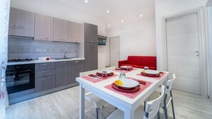 A modern kitchen with grey cabinets, a white countertop, and a red dining table set with plates and glasses. - Apartment with Sea View (TROPEA)