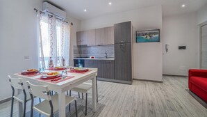 A modern kitchen with grey cabinets, a built-in oven, and a sink. There is a dining table with chairs and a red sofa in the living area. - Apartment with Sea View (TROPEA)