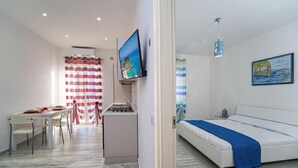 A modern hotel room with a bed, a desk, and a kitchenette.