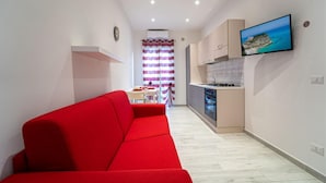 A modern apartment with a red sofa, a kitchen with a built-in oven, and a TV mounted on the wall.