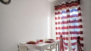 A dining area with a table set for two, chairs, and a window with striped curtains.